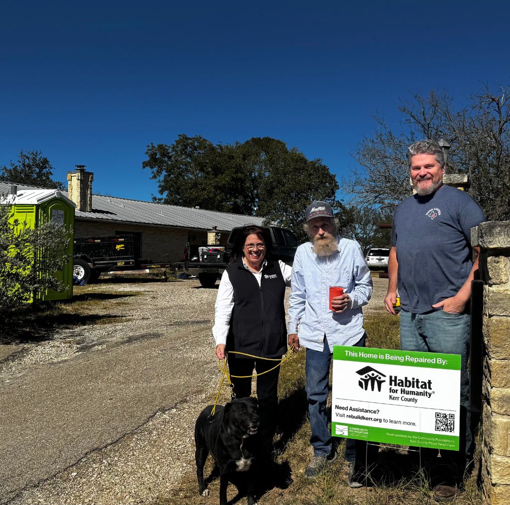 Three people and a dog standing by a sign infant of house.