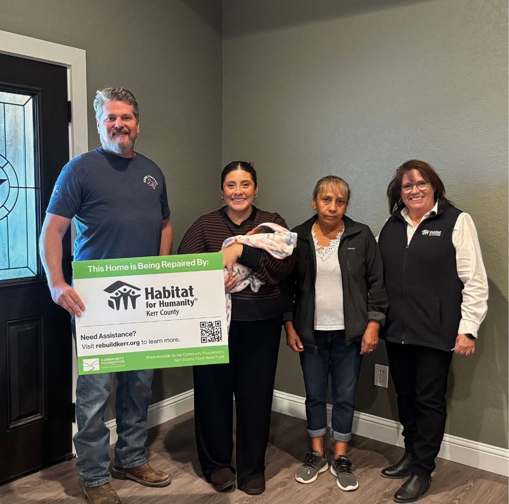 Four people inside of a house holding a sign.